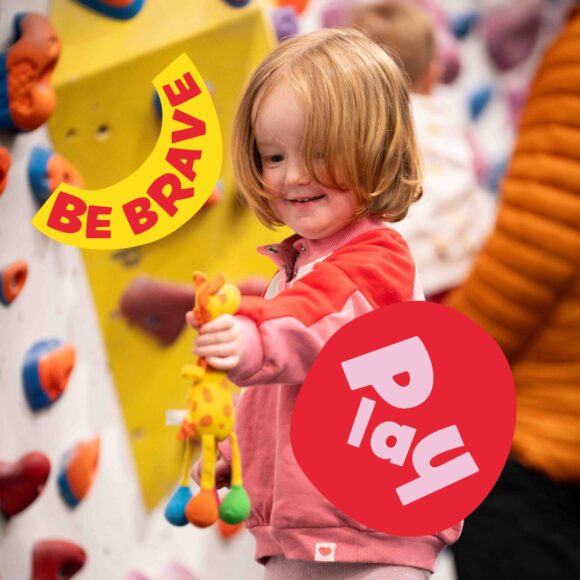 Depot Play participant holds a toy giraffe in front of a climbing wall