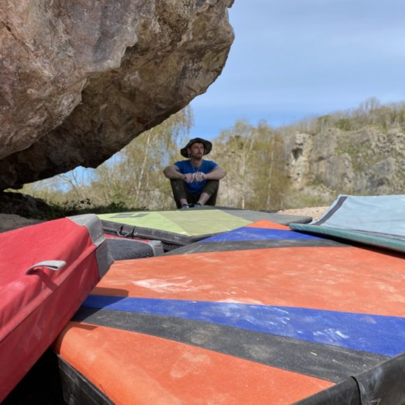 bouldering mat collection underneath a boulder with a climber resting