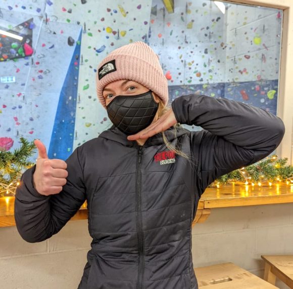 Female Depot Climbing staff member wearing a protective face mask gives the thumbs up to communicate key information