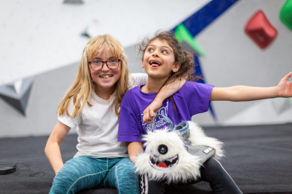 Two children sitting on the mats at a climbing centre smiling and making silly faces