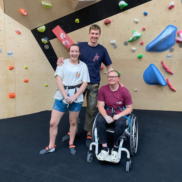 hannah morris and nathan betts of hannah morris bouldering pose for a photograph wiht lucy keyworth who is in a wheelchair at big depot leeds