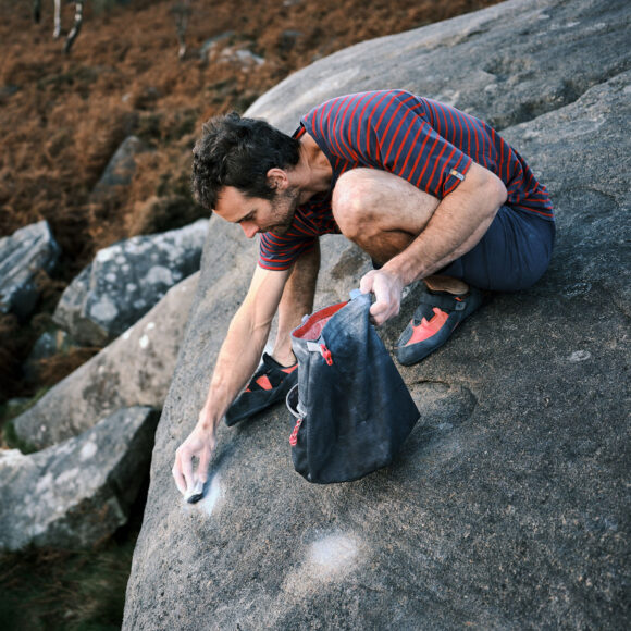 climber crouched on top of a boulder cleaning chalk after outdoor bouldering