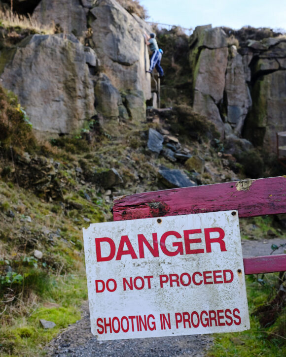 climber outdoor bouldering in the background of a sign that reads Danger do not proceed shooting in progress