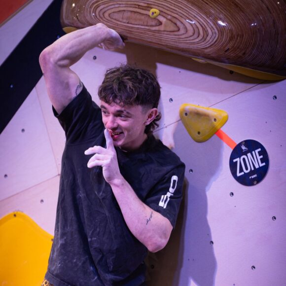 Max Milne shushes the crowd in a comical fashion at the top of a boulder