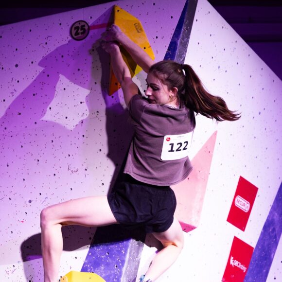 Emma Edwards matches the top hold of womens boulder 3 and looks down to the judge